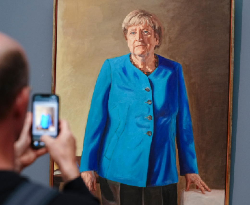 A visitor taking a photograph of Angela Merkel's portrait