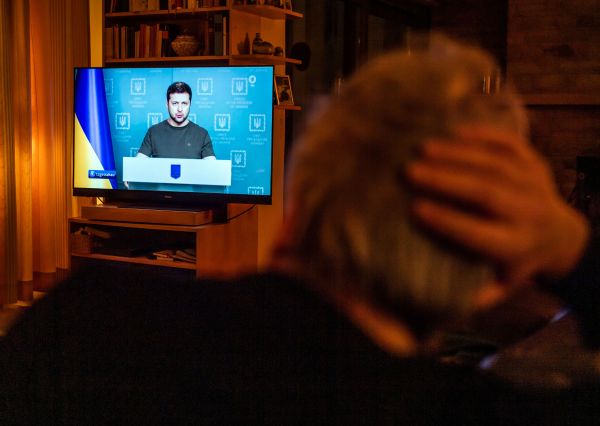 Mann sitzt vor Fernsehen, während die Tagesschau über den Ukrainekrieg berichtet.